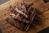 birds eye chilli beef jerky strips with some fat on the edges on a board with chilli flakes