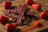 smoked paprika jerky strips on a board with dried paprika pods and paprika powder, but not too much powder on the strips
