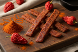 smoked paprika jerky strips on a board with dried paprika pods and paprika powder